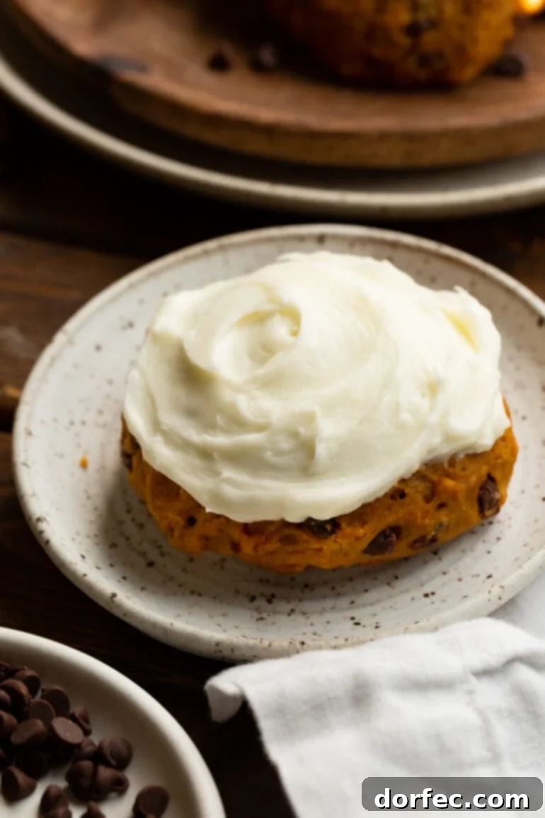A single, perfectly frosted pumpkin chocolate chip cookie rests on a small, elegant dessert plate, showcasing its soft texture and generous frosting.
