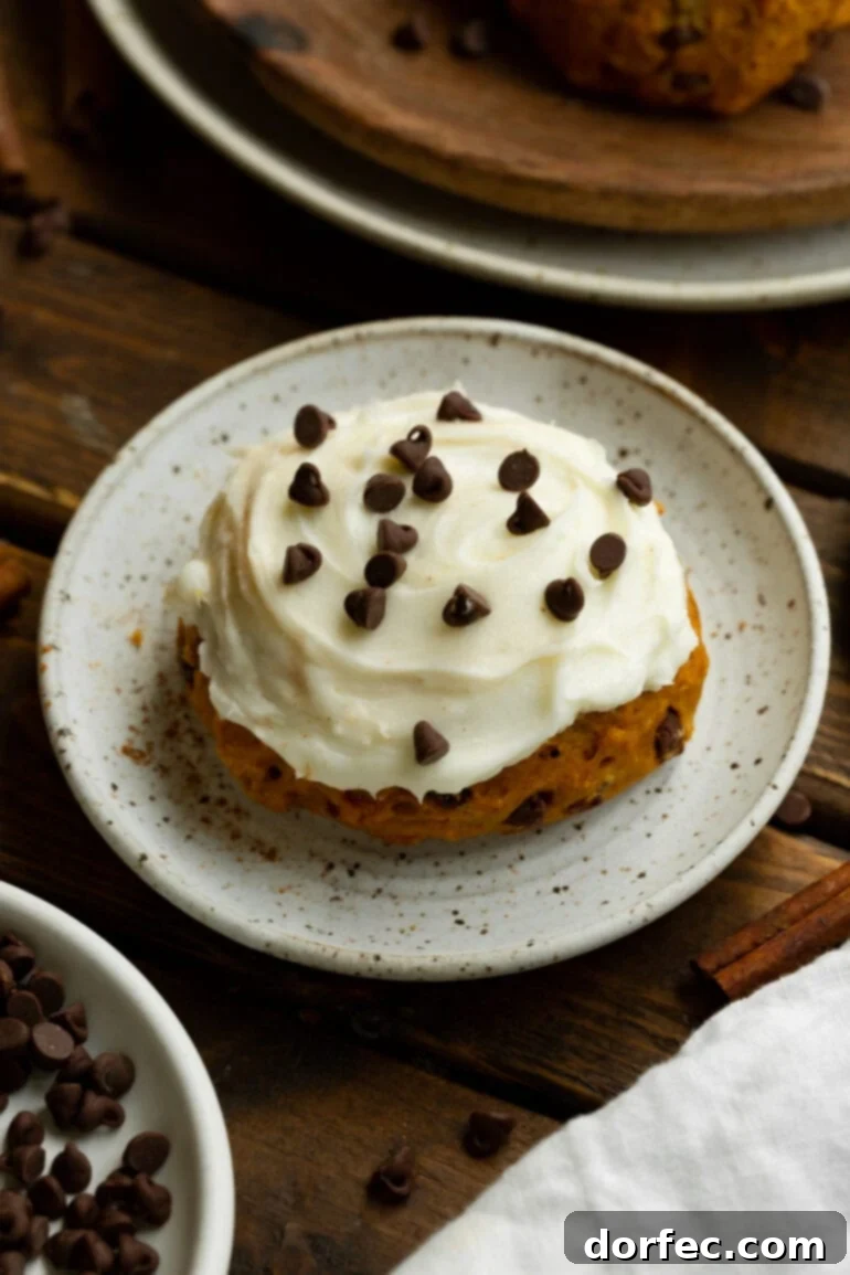 A close-up shot of a single, thick pumpkin chocolate chip cookie, topped with luscious cream cheese frosting and a sprinkle of mini chocolate chips, tempting you to take a bite.