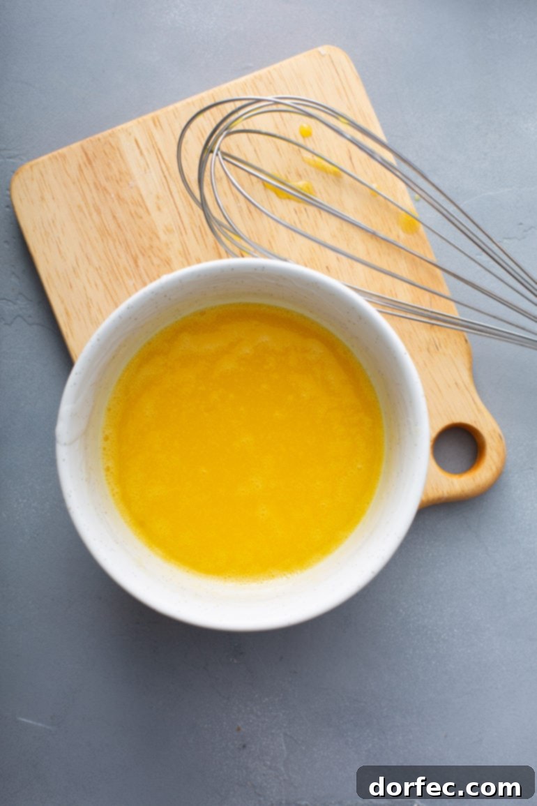 Family Recipe Lemon Meringue Pie 6 A bowl of egg yolks that have been whisked together. There is a wooden cutting board and a whisk by the bowl of egg yolks.