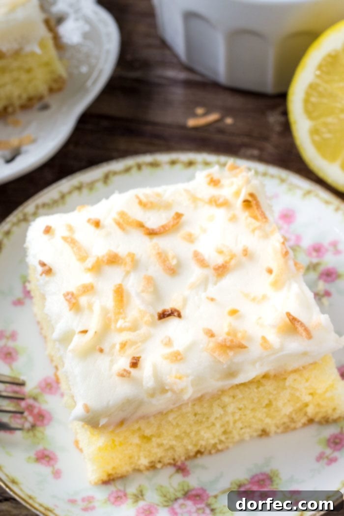 A beautifully sliced lemon coconut cake, showcasing its moist texture and topped with airy coconut frosting and toasted coconut flakes.