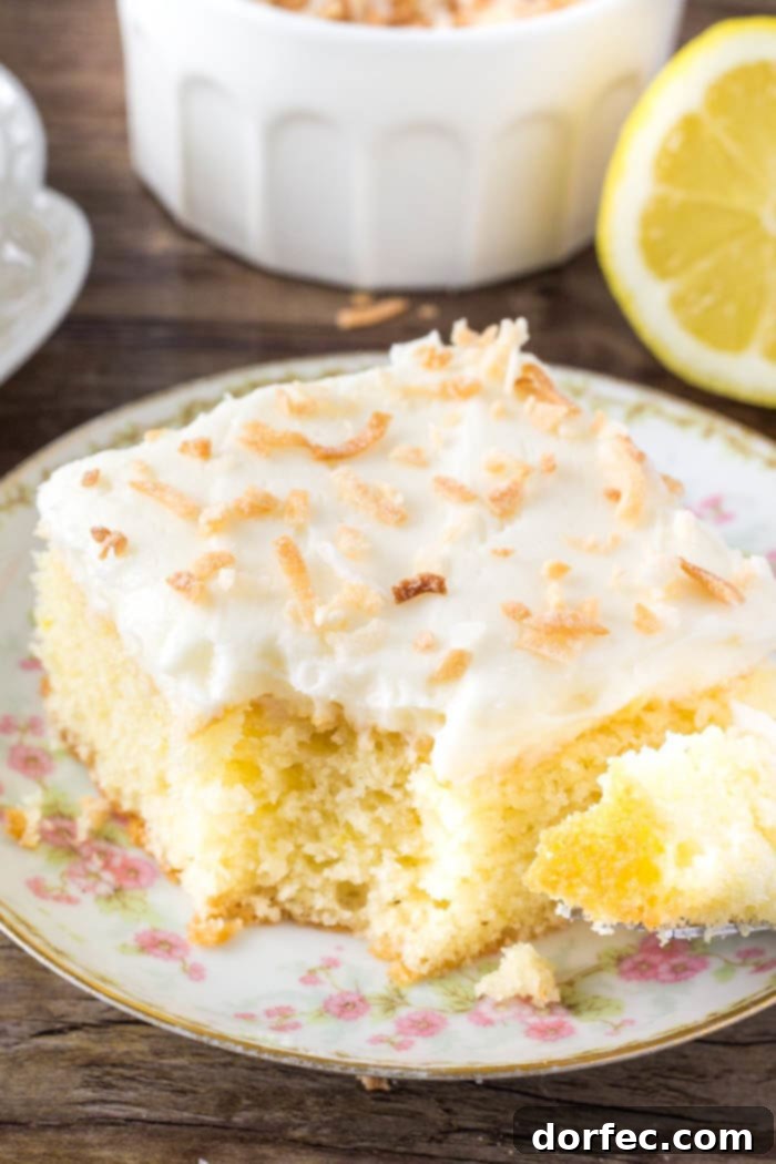 A close-up of a moist, tender slice of lemon cake generously covered with creamy coconut frosting.