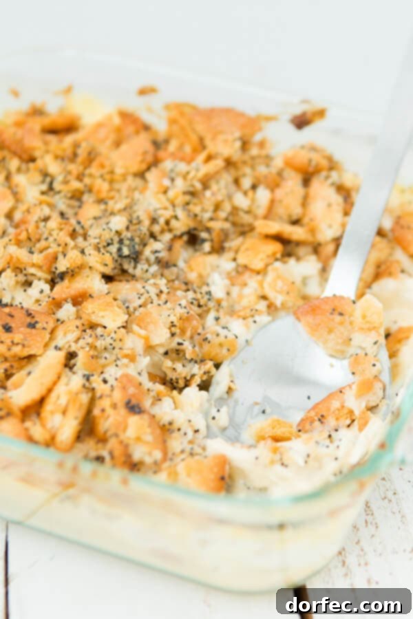 Scooping out a generous portion of everyone's favorite creamy Poppy Seed Chicken Casserole. A serving spoon scoops out a portion of Poppy Seed Chicken Casserole from a glass baking dish, revealing its creamy interior and crunchy topping.