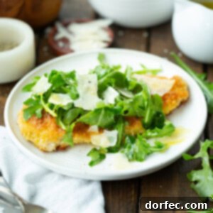 A vibrant close-up of the finished Lightened Up Chicken Parm, with crispy chicken, fresh greens, and Parmesan shavings.