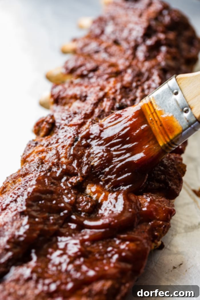 A baking sheet with a rack of ribs and a basting brush slathering on bbq sauce to make the smoky bbq instant pot ribs recipe