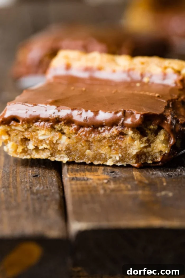A single, delectable peanut butter bar generously topped with smooth chocolate frosting, resting on a wooden table.