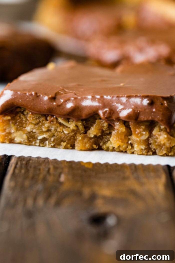 A close-up shot of a single peanut butter bar topped with thick chocolate frosting, resting on a piece of parchment paper.