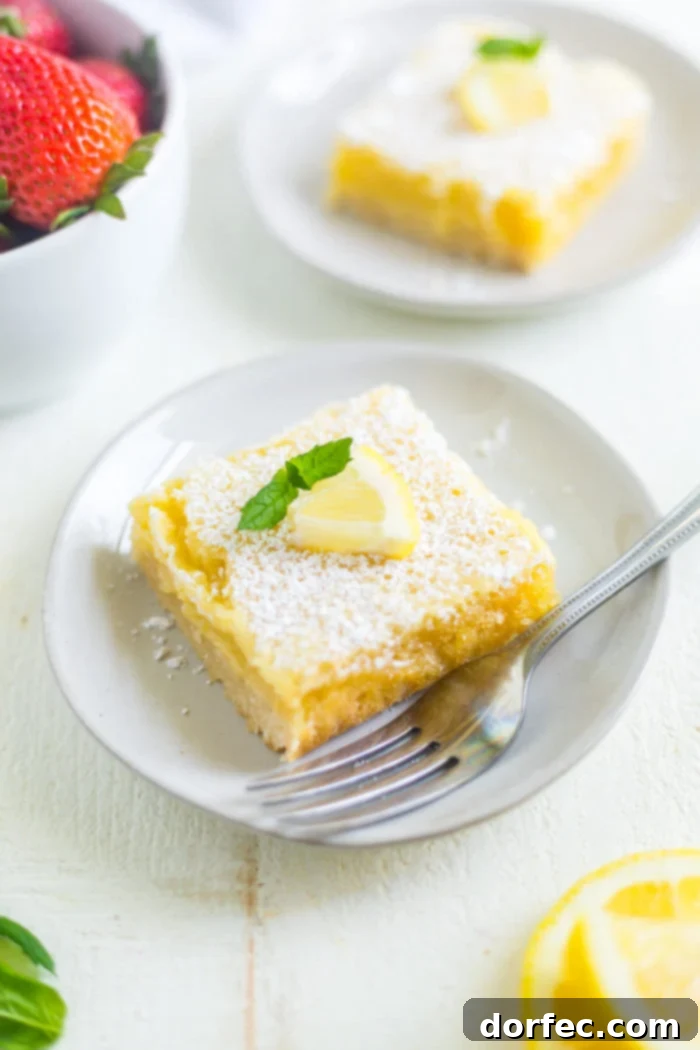 recipe for lemon bars a photo of a single square lemon bar topped with powdered sugar and a wedge of lemon sitting on a small white dessert plate with a fork sitting next to it