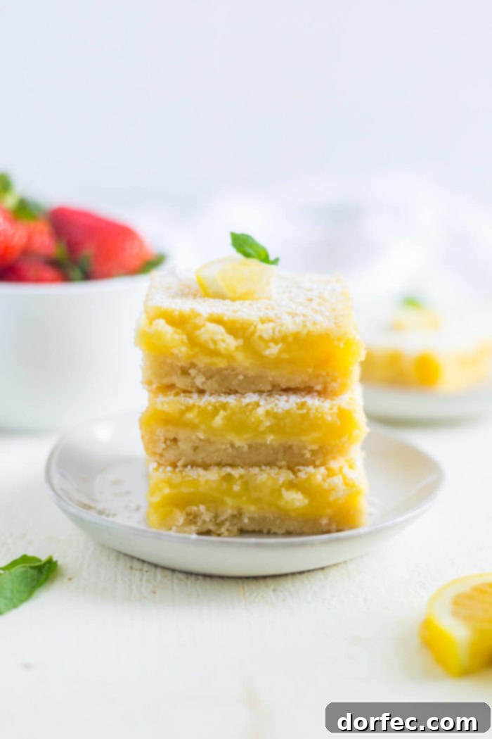 lemon bars a photo of three square lemon bars stacked on top of each other sitting on a small white dessert plate
