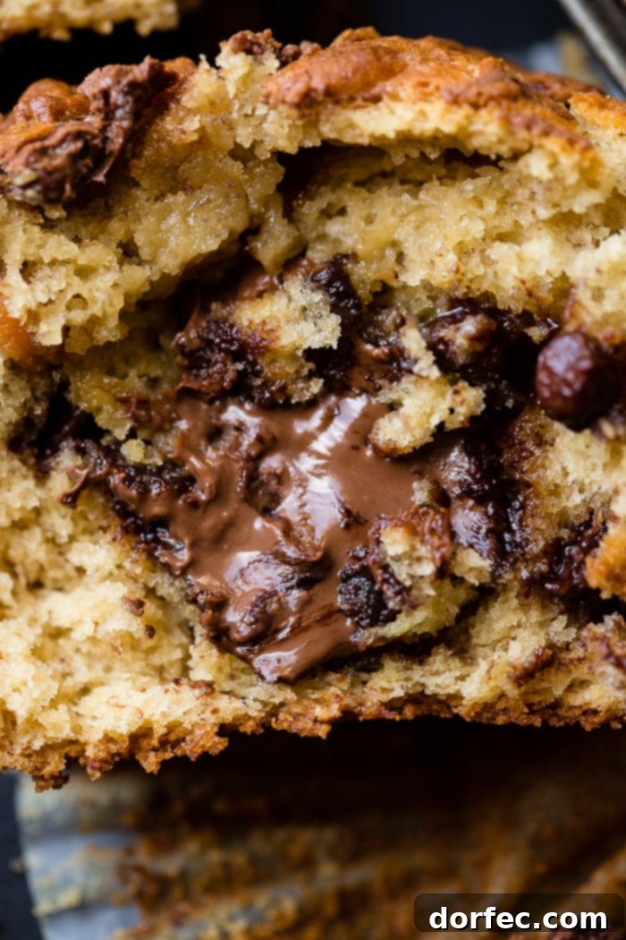 Nutella Surprise Peanut Butter Banana Muffins 8 A perfectly sliced Nutella stuffed peanut butter banana muffin, showcasing the molten Nutella core, rests on an open muffin liner. An inviting visual for breakfast, lunch, dinner, or dessert.