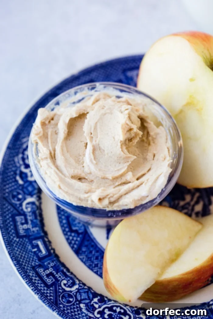 A close-up shot of a blue dish with a sliced red apple and a whole half apple, accompanied by a small container of healthy peanut butter Greek yogurt dip, highlighting its creamy texture.