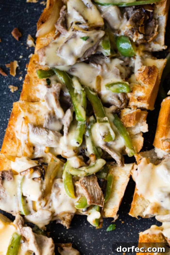 Philly Cheesesteak Stuffed Loaf 3 A close-up shot of a French bread loaf, split lengthwise and overflowing with thinly sliced, seasoned steak, vibrant bell peppers, caramelized onions, and creamy melted cheese sauce, creating an irresistible easy Philly Cheesesteak bread.