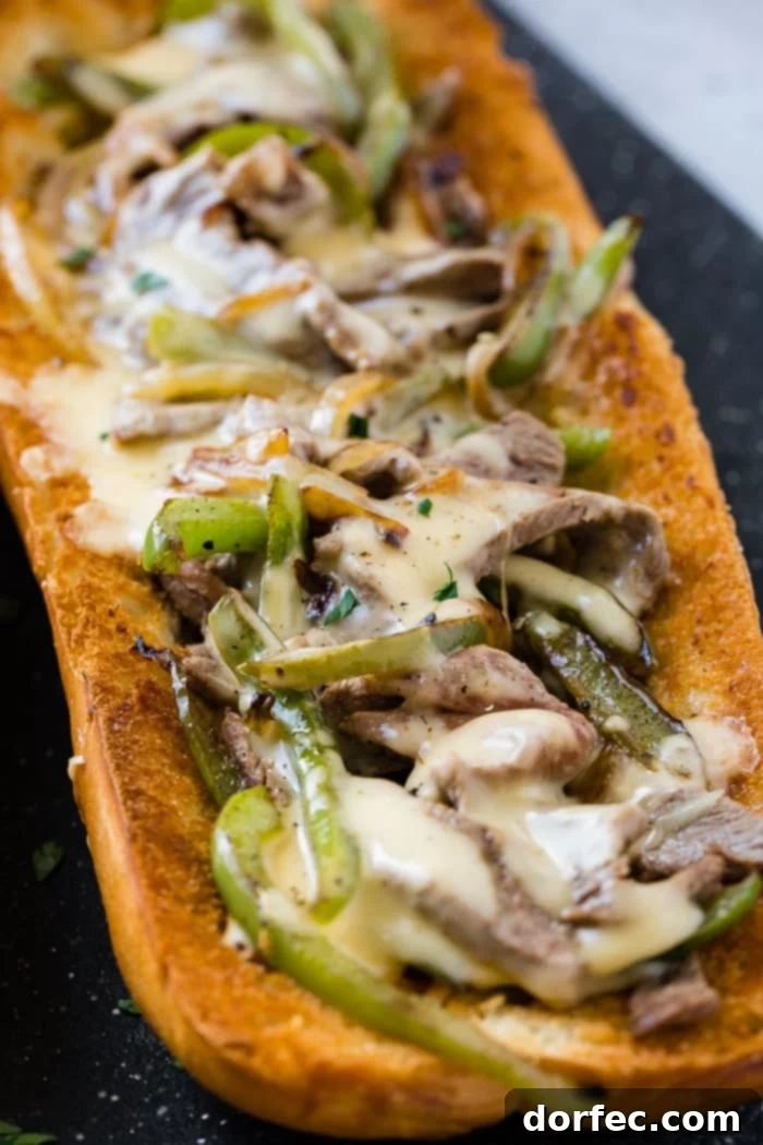 Philly Cheesesteak Stuffed Loaf 4 Detailed view of a French bread loaf, cut open and generously filled with finely sliced steak, sautéed bell peppers, sweet onions, and a luscious cheese sauce, creating an inviting and easy Philly Cheesesteak recipe.