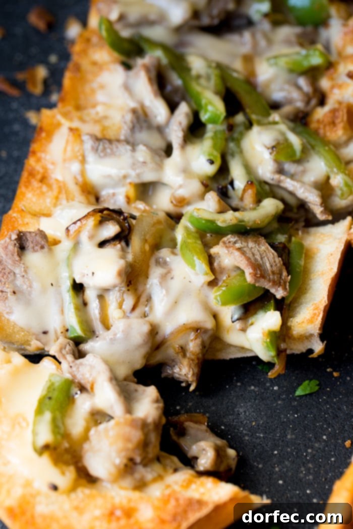 Philly Cheesesteak Stuffed Loaf 5 A beautifully presented French bread loaf, sliced open and generously filled with perfectly cooked steak, colorful bell peppers, caramelized onions, and a decadent cheese sauce, showcasing an easy Philly Cheesesteak recipe ready to be enjoyed.