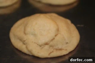 A perfectly baked, golden-brown Milky Way cookie with visible chocolate and caramel swirls, sitting on a parchment-lined baking sheet, promising a delightful treat.