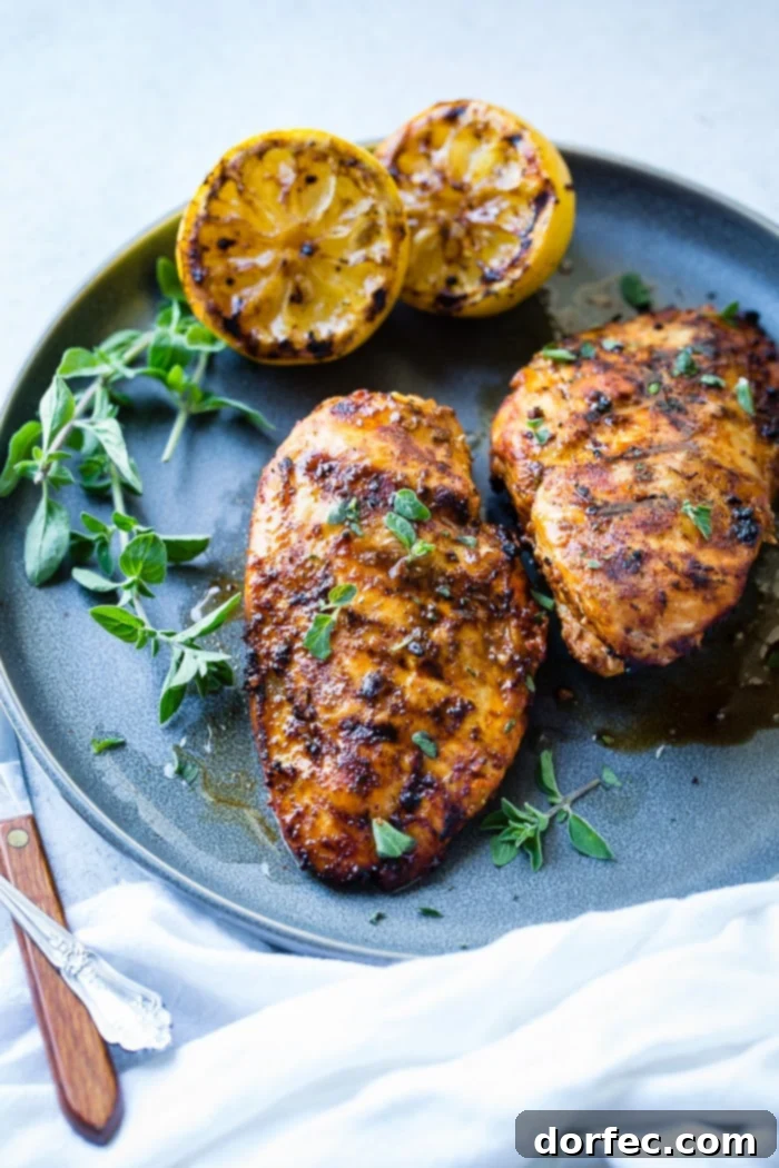 Speedy Oregano Grilled Chicken 4 A grey plate with a sliced quick grilled chicken with oregano with oregano and grilled lemons behind it