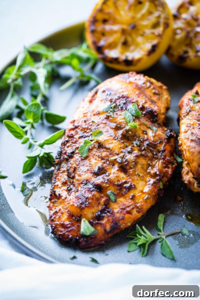 Speedy Oregano Grilled Chicken 5 A grey plate with a sliced quick grilled chicken with oregano with oregano and grilled lemons behind it and sitting on a white napkin