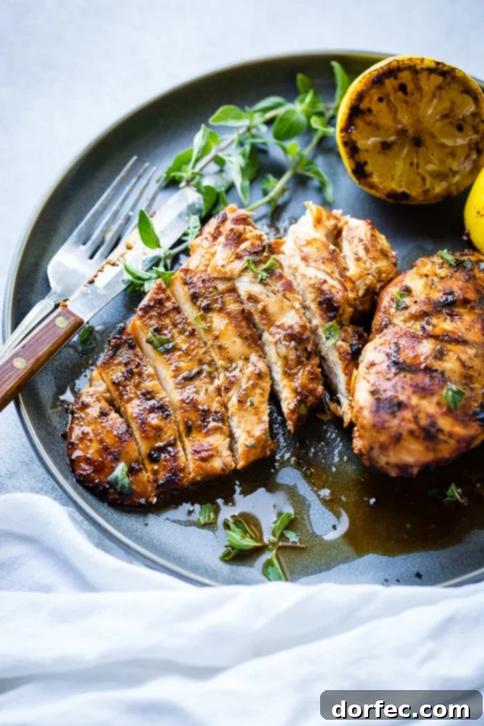 Speedy Oregano Grilled Chicken 7 A grey plate with a sliced quick grilled chicken with oregano with oregano and grilled lemons behind it and sitting on a white napkin
