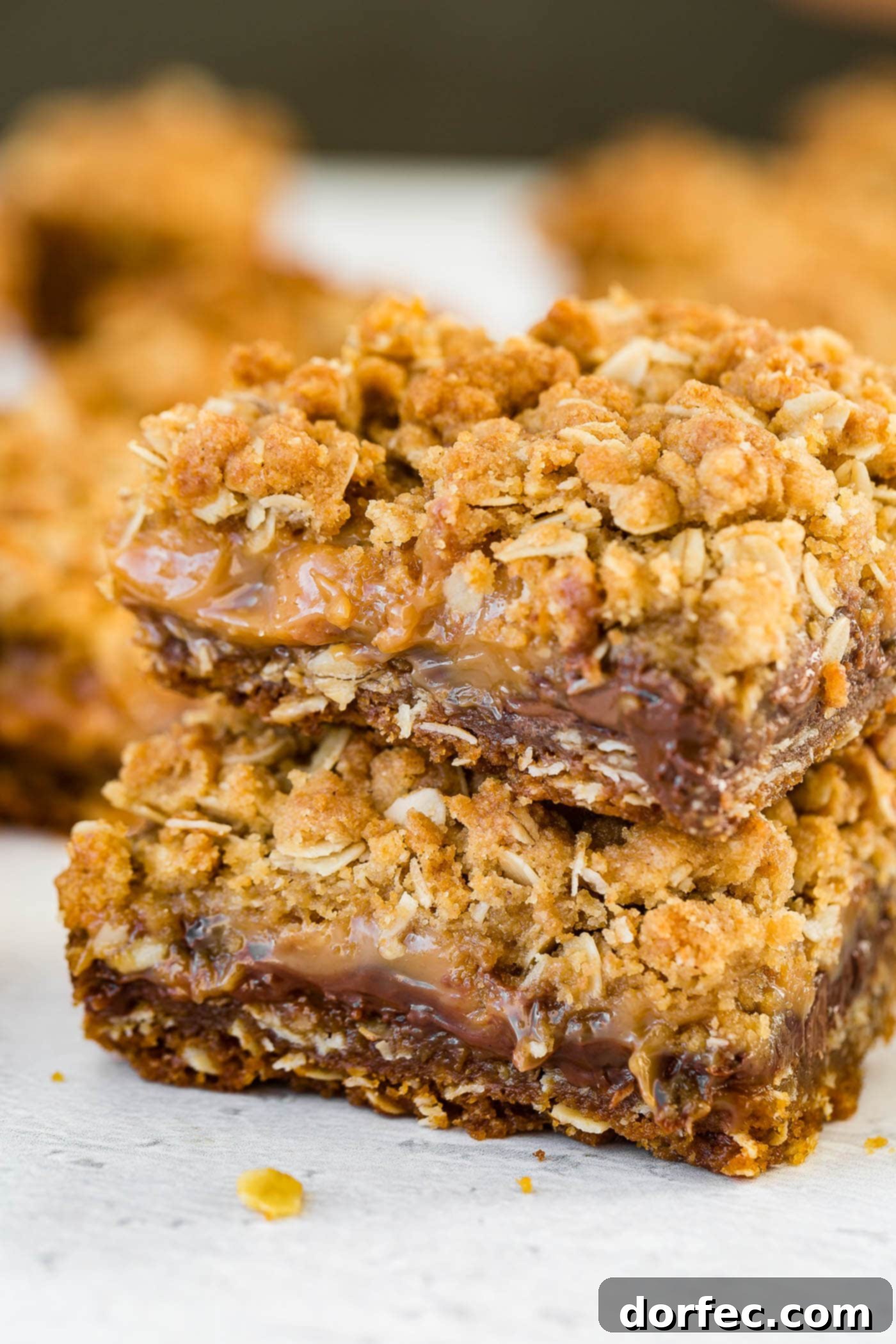 A close-up photo of two oatmeal Carmelita bars with gooey caramel and silky chocolate visible between the oat layers, placed on a rustic wooden surface.