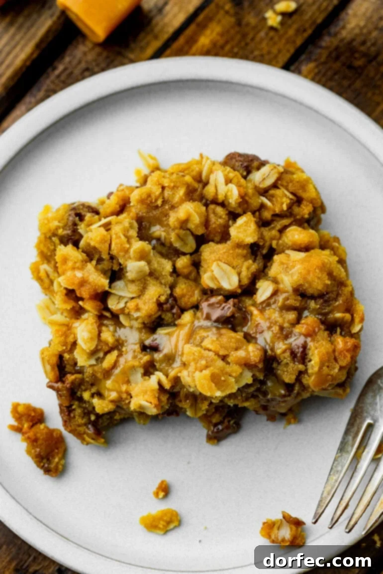 A close-up photo of a single Carmelitas bar with a golden crumble topping, gooey caramel, and melted chocolate, resting on a small white dessert plate.