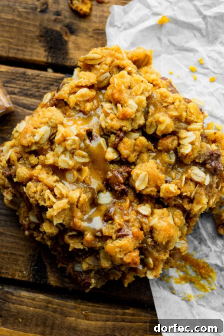 A close-up image of a single Carmelita bar, highlighting its golden oat crumble topping and the visible layers of gooey chocolate and caramel underneath.