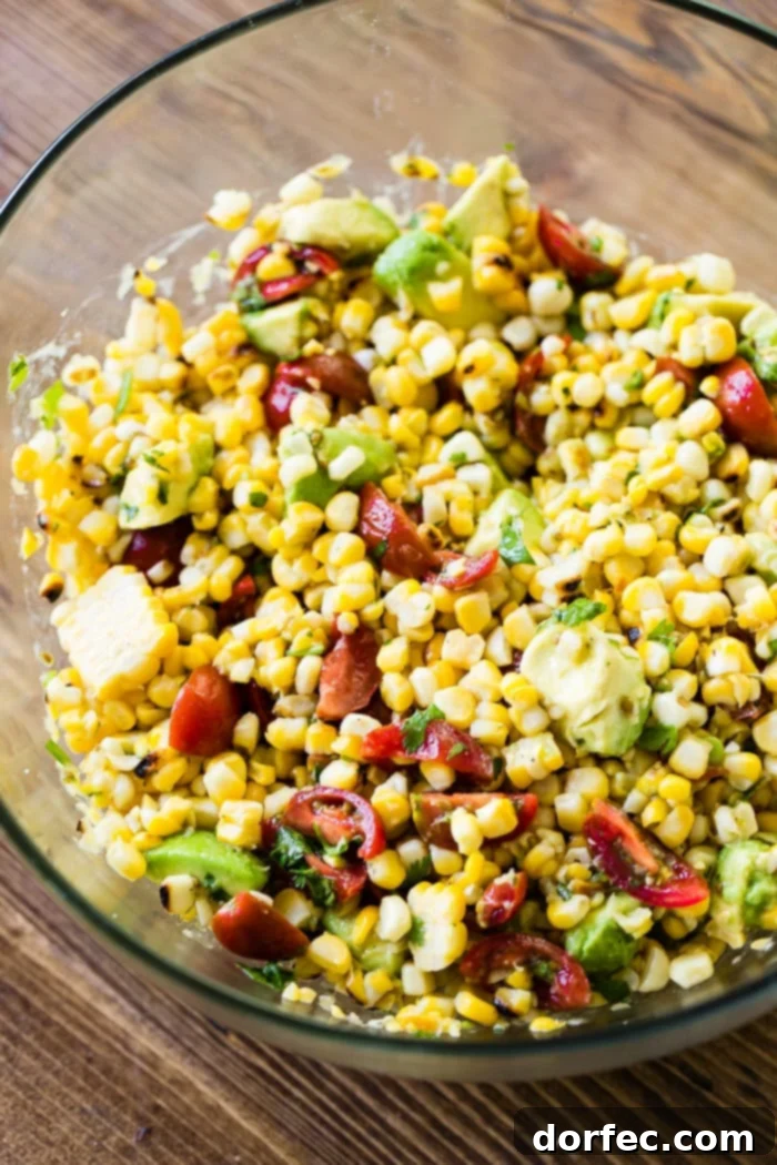 A close-up shot of a generously portioned glass bowl filled with a fresh grilled corn salad, vibrant with tomatoes and creamy avocados, ready to be served.