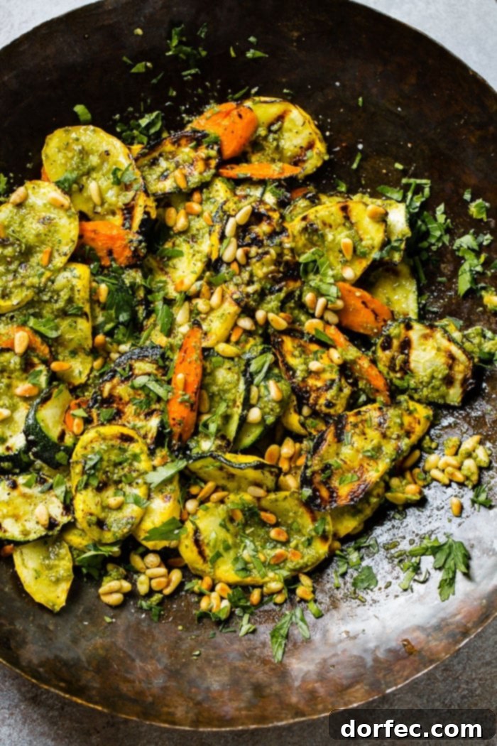 Another close-up shot of grilled vegetables, beautifully arranged with pesto, fresh parsley, and toasted pine nuts. The vibrant mix of zucchini, yellow squash, and carrots highlights the appeal of this quick 15-minute grilled veggies with pesto recipe.