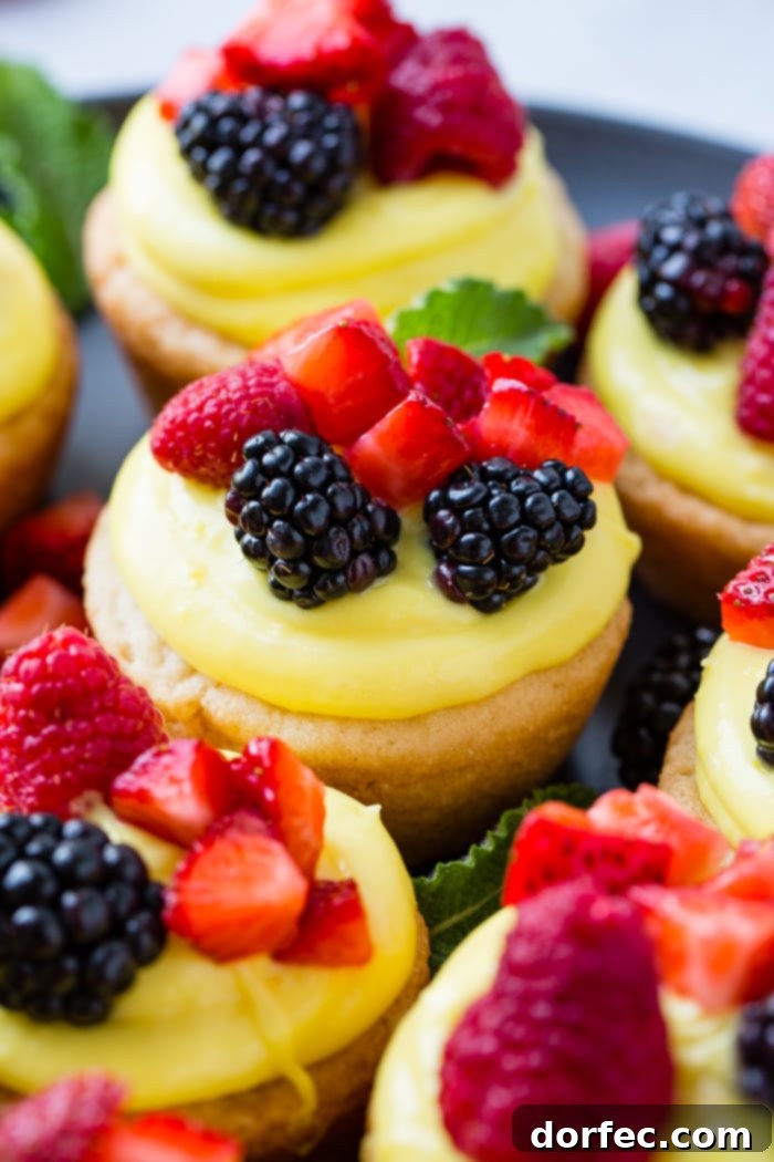 Sunshine Lemon Sugar Cookie Bites 2 A dark pan with sugar cookie cups filled with lemon filling and topped with blackberries, raspberries and chopped strawberries, ready to serve as a summer dessert.