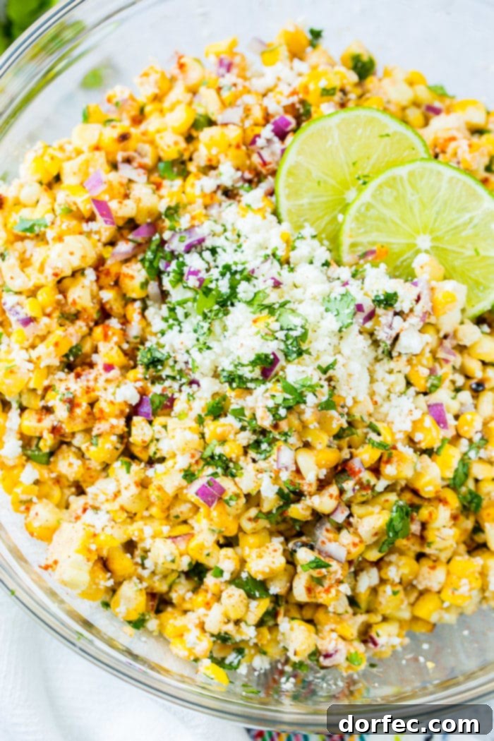 A glass bowl full of grilled corn, red onions, cilantro, creamy Mexican crema, crumbled cotija cheese and fresh lime juice which makes the best Elote Mexican Grilled Corn Salad, a vibrant and flavorful side dish.