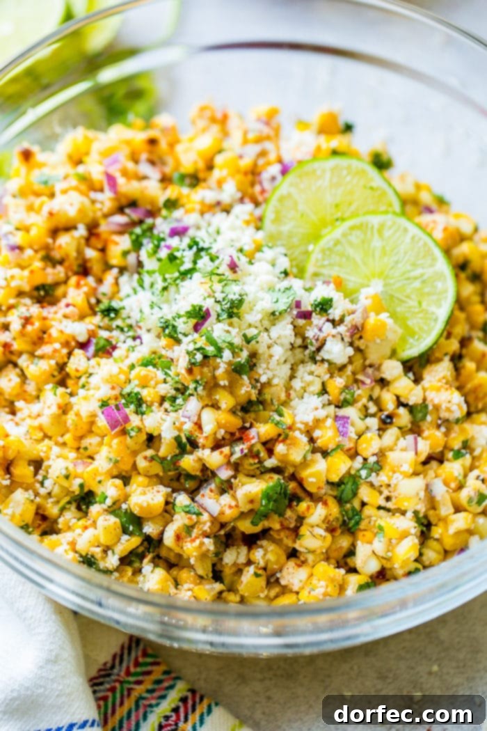 Grilled corn, red onions, cilantro, creamy crema, cotija cheese, and a drizzle of lime juice in a heaping mound inside a bowl, ready to be served as a vibrant side.