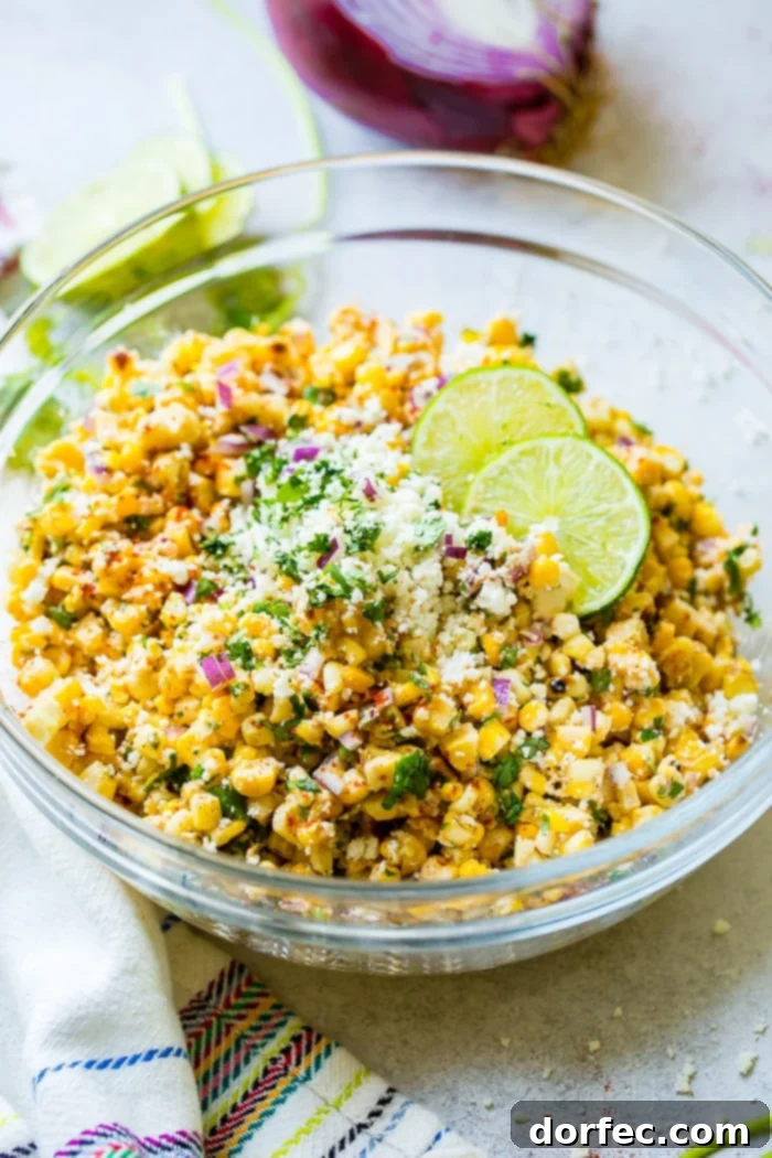 A glass bowl filled with grilled corn, red onions, cilantro, creamy crema, cotija cheese, and zesty lime juice, presenting a tempting Elote Mexican Corn Salad.