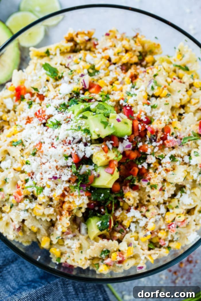 A close up photo of a bow tie pasta salad with avocados, peppers, grilled corn, cilantro, and cotija cheese making up an Elote Mexican Corn Pasta Salad