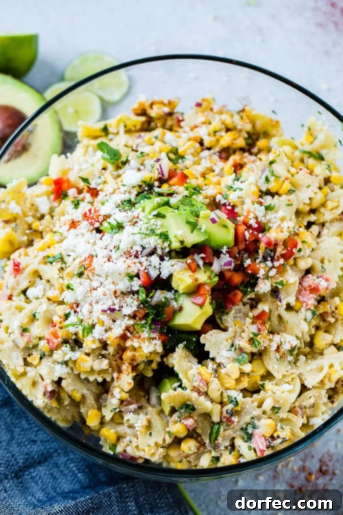 A close up photo of a bow tie pasta salad with avocados, peppers, grilled corn, cilantro, and cotija cheese making up an Elote Mexican Corn Pasta Salad