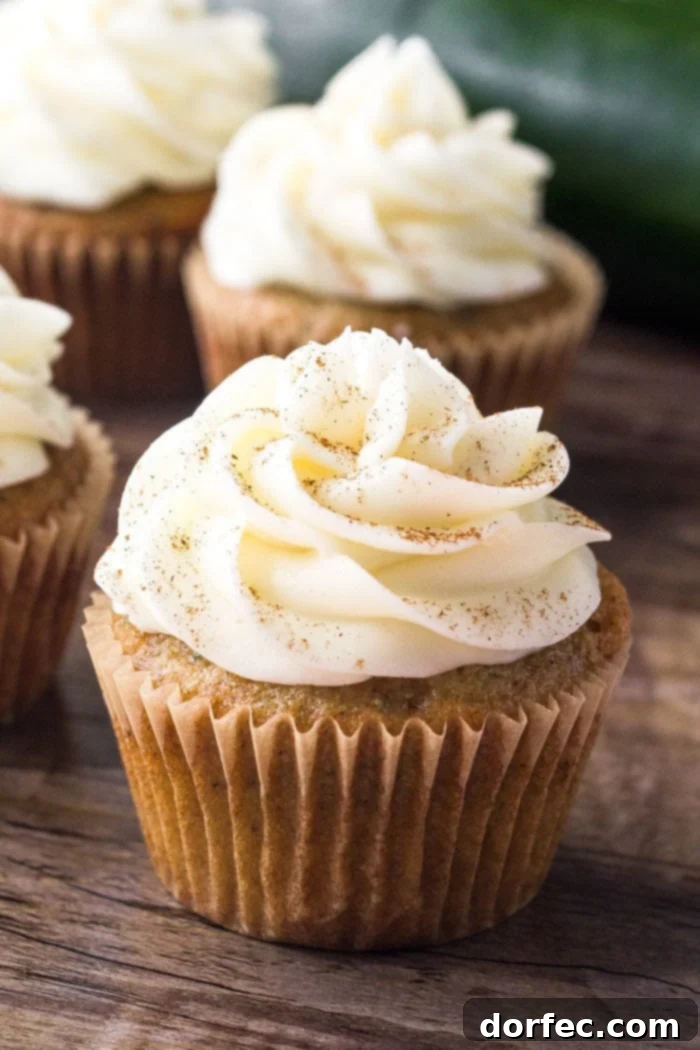 A freshly baked zucchini cupcake in a wrapper, generously topped with fluffy cream cheese buttercream frosting and a sprinkle of cinnamon, ready to be enjoyed.
