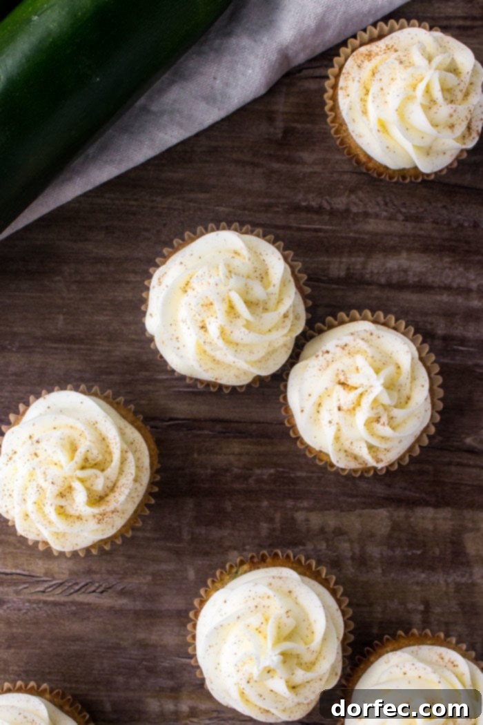 An overhead view of several zucchini cupcakes, beautifully frosted with cream cheese buttercream and lightly sprinkled with cinnamon, arranged on a rustic wooden surface.