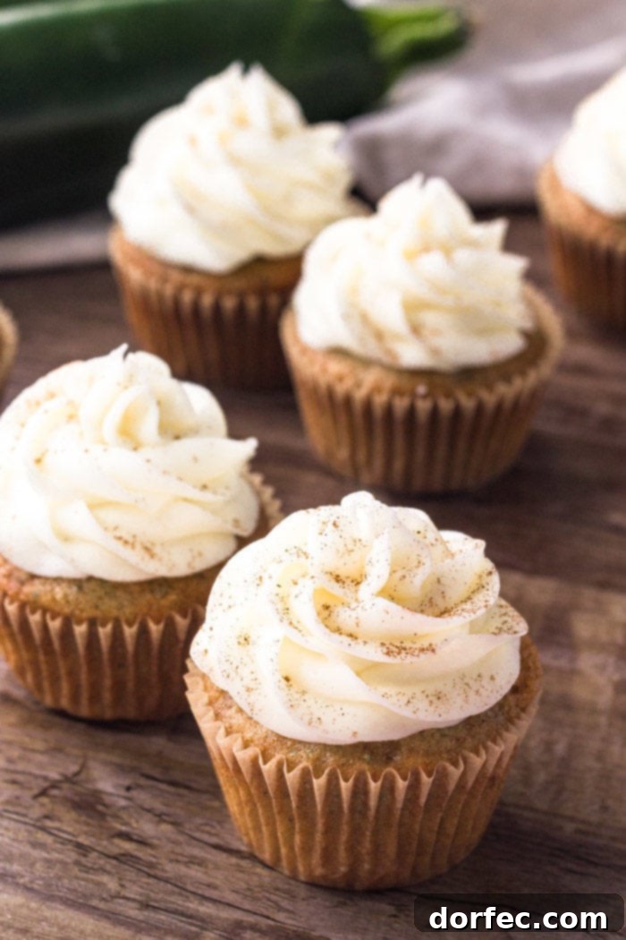 A close-up of two zucchini cupcakes, crowned with swirls of cream cheese frosting and a delicate dusting of cinnamon, inviting a taste.
