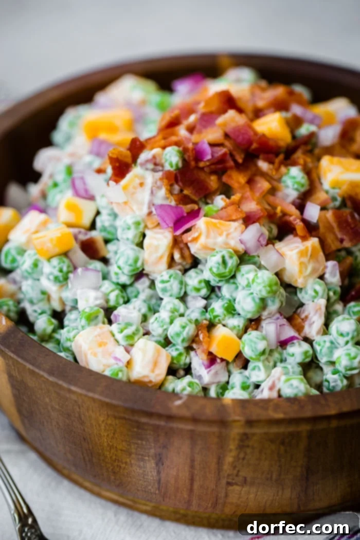 a wooden bowl full of creamy southern english pea salad with bacon, chunks of colby jack cheese