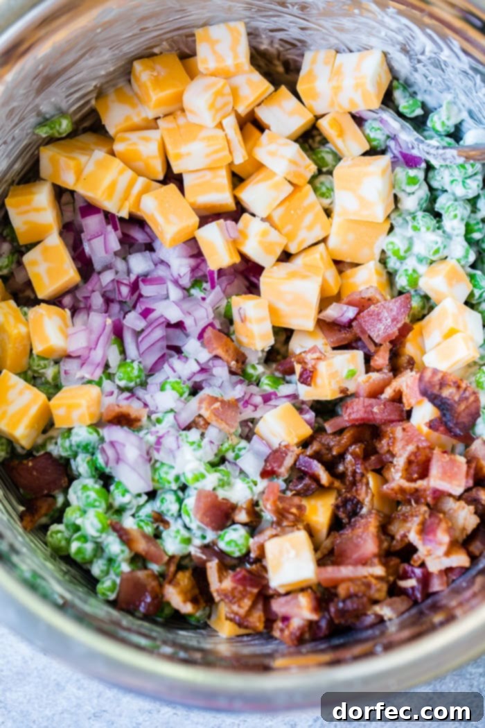 a metal bowl full of creamy southern english pea salad with bacon, chunks of colby jack cheese