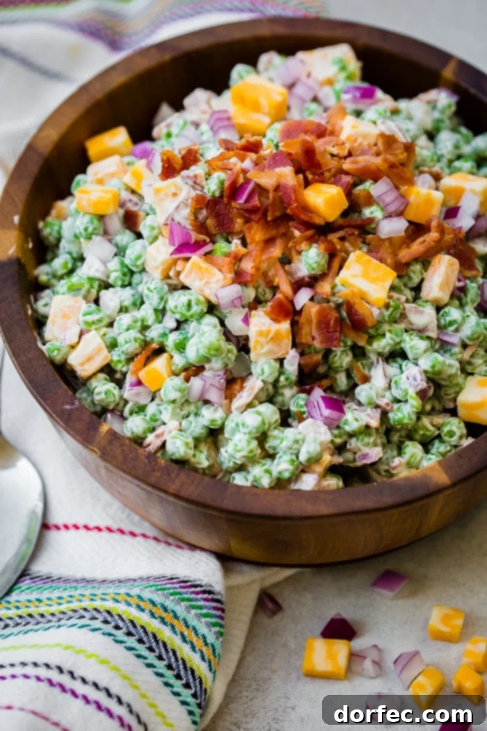 a wooden bowl full of creamy southern english pea salad with bacon, chunks of colby jack cheese and a metal spoon sitting on the side