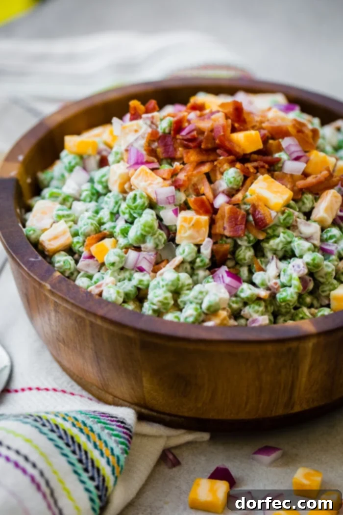 a wooden bowl full of creamy southern english pea salad with bacon, chunks of colby jack cheese