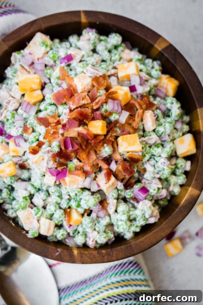 a wooden bowl full of creamy southern english pea salad with bacon, chunks of colby jack cheese