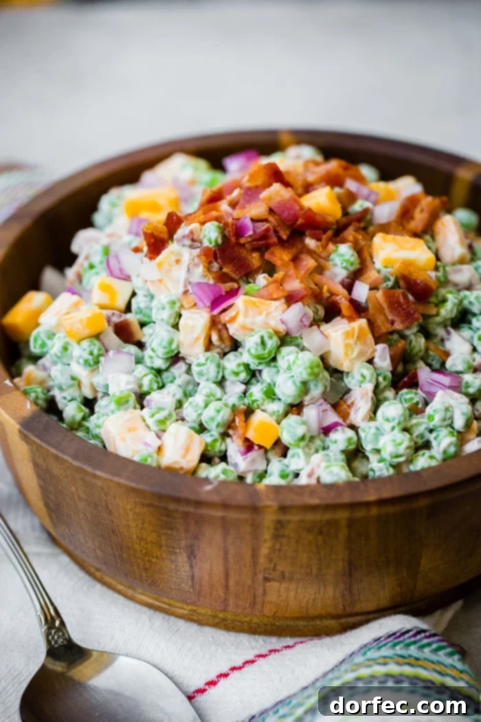 a wooden bowl full of creamy southern english pea salad with bacon, chunks of colby jack cheese