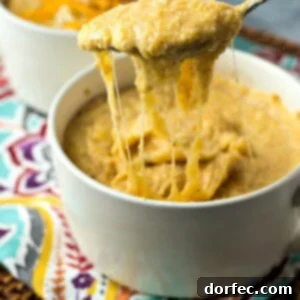 A white bowl full of cheesy grits and a spoon lifting it out of the bowl, showing the creamy texture