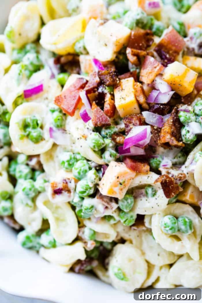 Creamy orchiette pasta salad with English peas, bacon, Colby Jack cheese, and red onion in a white bowl, perfect for Southern potlucks.