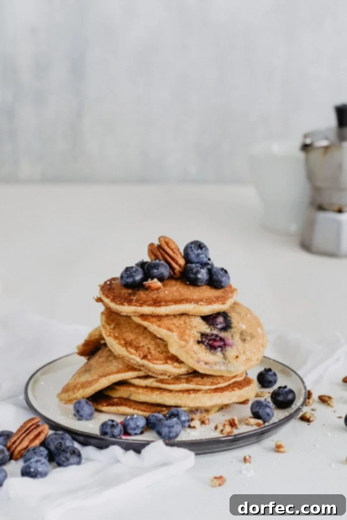 An artistic overhead shot capturing a stack of golden brown blueberry pecan pancakes, elegantly garnished with a light dusting of powdered sugar, fresh blueberries, and perfectly toasted pecan halves, evoking a sense of gourmet indulgence.