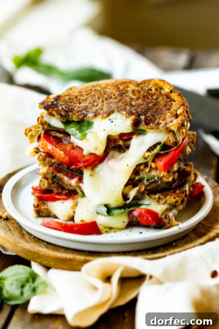 A stack of golden-brown grilled cheese sandwiches, each oozing with melted Havarti cheese, fresh tomato, and basil. They are piled high on a white serving plate, inviting you to grab one.