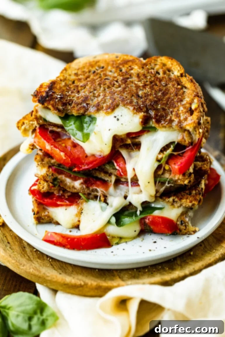 A stack of four halves of melty tomato basil grilled cheese sandwiches, neatly arranged on a white plate, showcasing the golden bread and vibrant fillings.