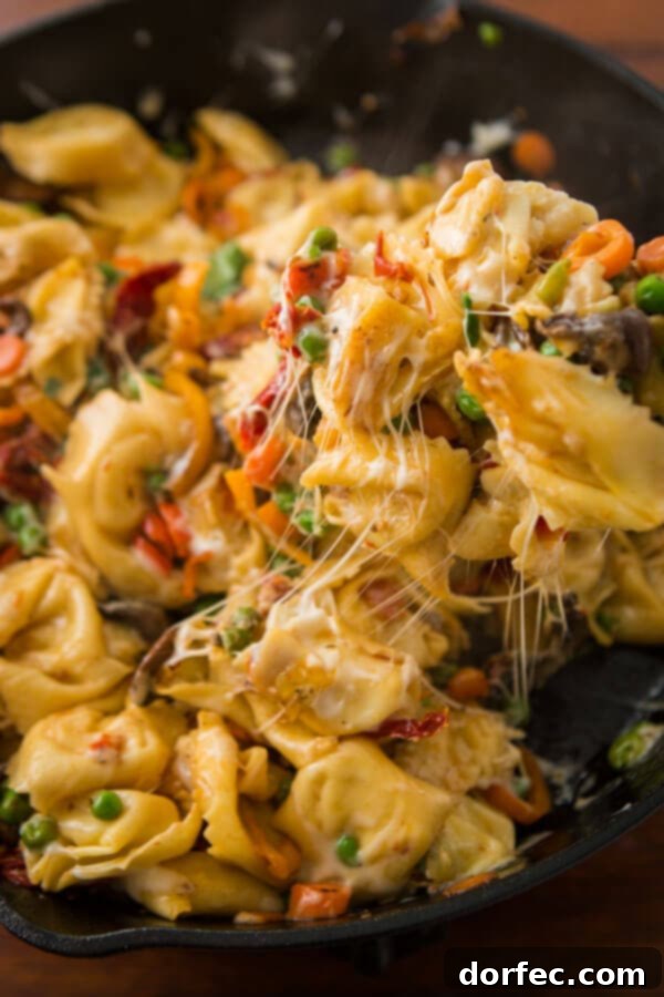 Perfectly cooked tortellini being added to a skillet with sautéed vegetables for cheesy pan fried tortellini