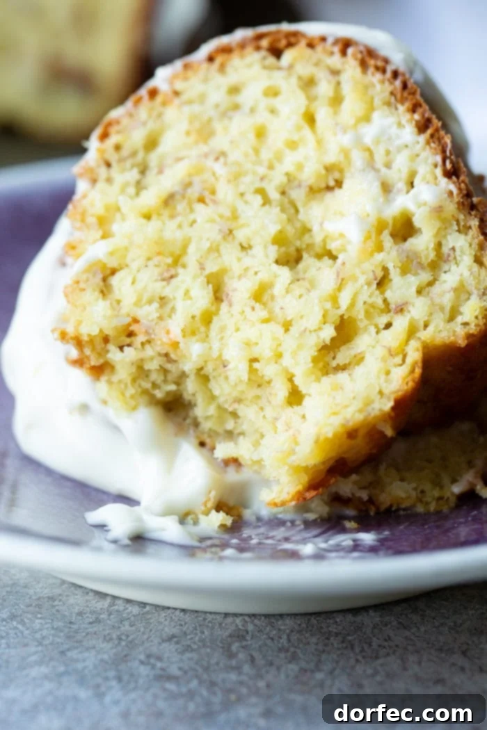 Heavenly Banana Bundt Cake 9 A slice of banana bundt cake with white creamy frosting on a blue plate.