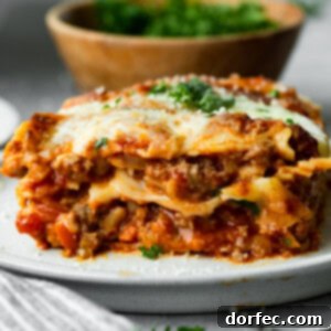 a photo of a serving of layered hearty meat lasagna on a white plate topped with melted cheese and chopped parsley