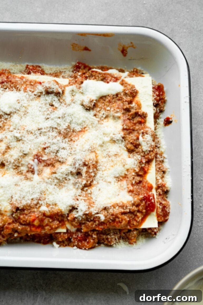 a photo of lasagna being assembled in a baking dish with layers of meat sauce, noodles, and cheese